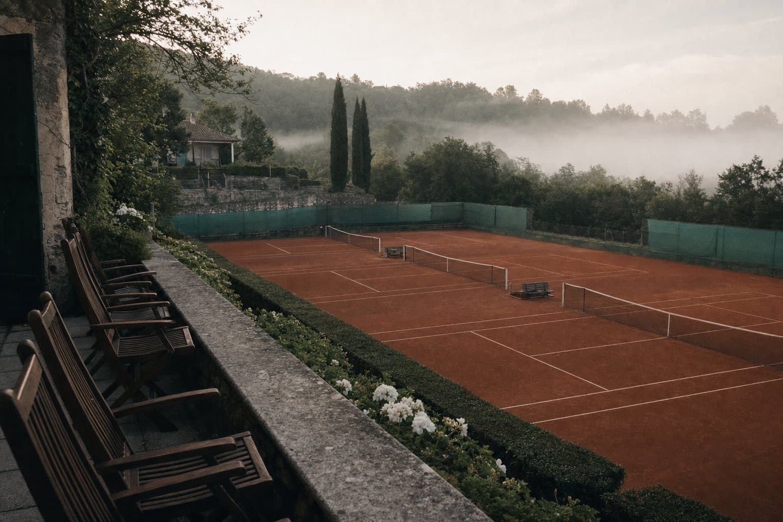A quiet European clay-court tennis club seen from the clubhouse terrace in morning light.